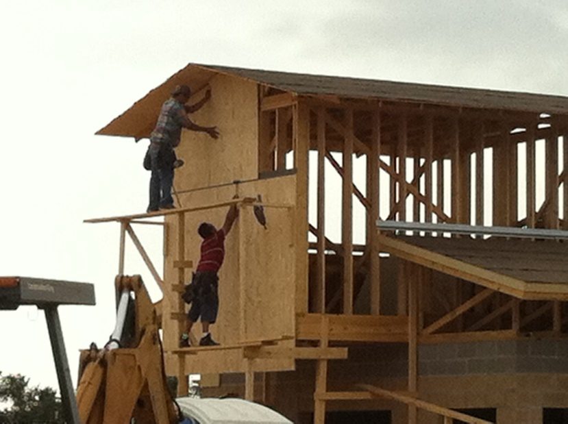 Two carpenters installing sheathing on a wood-framed house