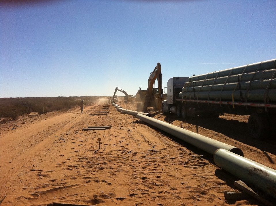 Pipeline string along a dirt road with excavators and a pipe truck