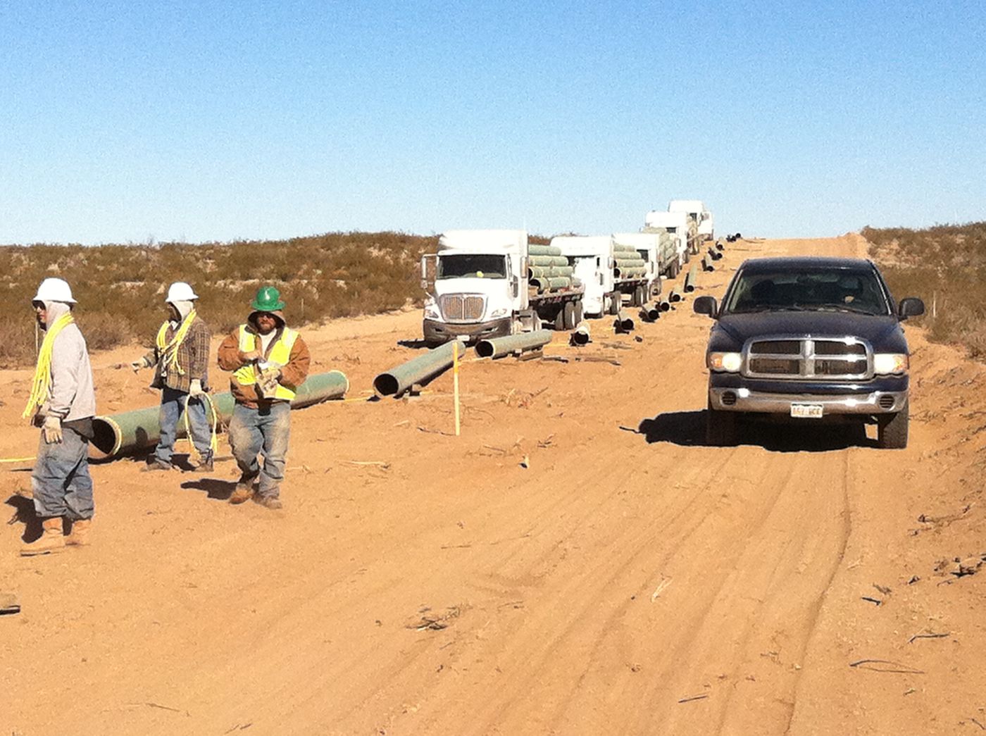 Pipeline crew and pipe trucks on a desert right-of-way