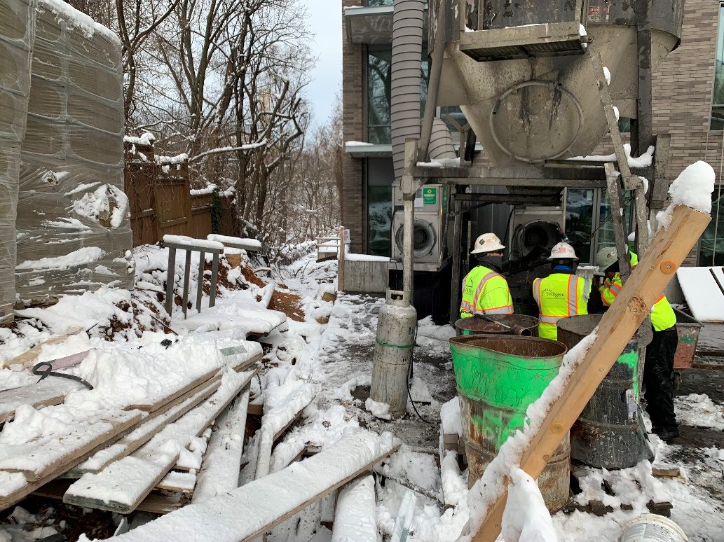 Crew working mechanical equipment in snow beside a building